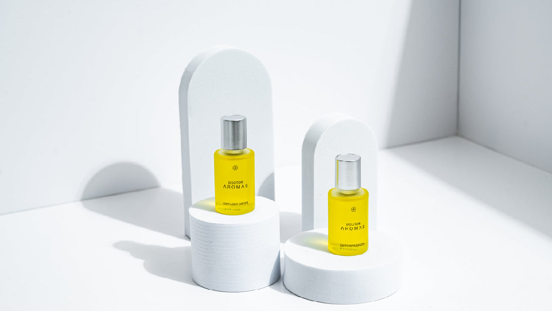 Two yellow Doctor Aromas diffuser oil bottles displayed on rounded white platforms with soft shadows and minimalist arches in a bright, white setting.