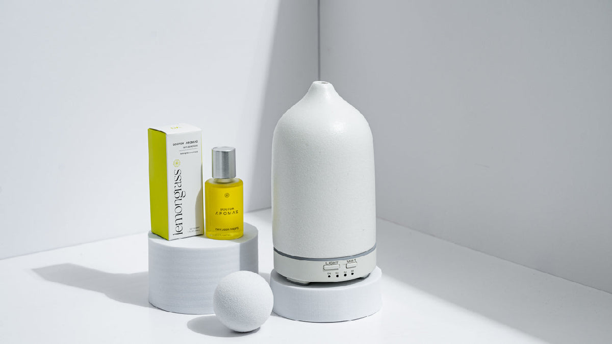 Doctor Aromas Lemongrass diffuser oil with packaging, displayed next to a modern white ceramic ultrasonic diffuser on minimalist white platforms.