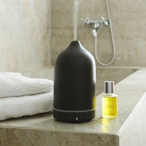 Matte black ceramic essential oil diffuser with yellow oil bottle on marble bathroom counter with white towels. - The Gift of HOPE® Deluxe - White - Doctor Aromas