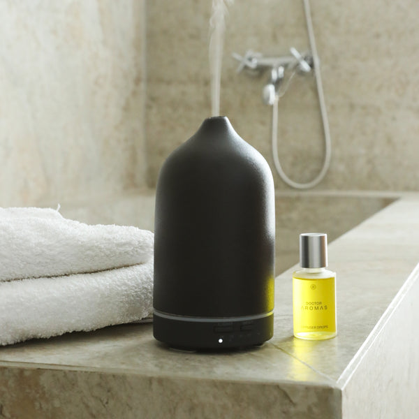 Matte black ceramic essential oil diffuser with yellow oil bottle on marble bathroom counter with white towels. - The Gift of HOPE® Deluxe - White - Doctor Aromas