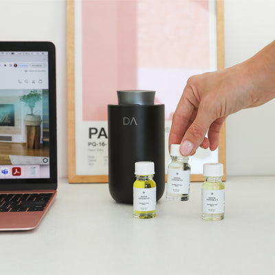 Three small essential oil refill bottles with white labels beside a sleek black portable diffuser on a white surface. - Portable Diffuser Refills Pack of Three | Signature Collection - Signature Collection - Doctor Aromas