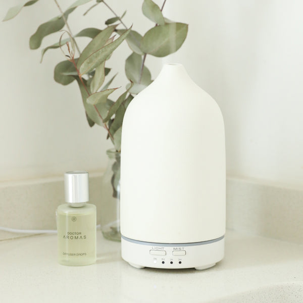 White ceramic essential oil diffuser with rounded top and control buttons on base beside a small bottle of oil and. - The Gift of HOPE® Deluxe - White - Doctor Aromas