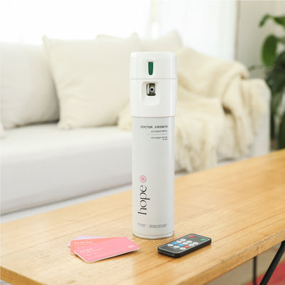 White cylindrical A/C scenting spray labeled "Hope," accompanied by a black remote and two pink scent cards on a wooden. - A/C Scenting System | Blush - Blush - Doctor Aromas