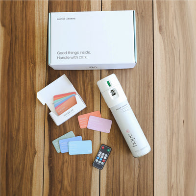 White sleek A/C scenting device with Pomelo scent cards in pastel colors and a black remote on wooden surface, white box in. - A/C Scenting System | Pomelo - Pomelo - Doctor Aromas