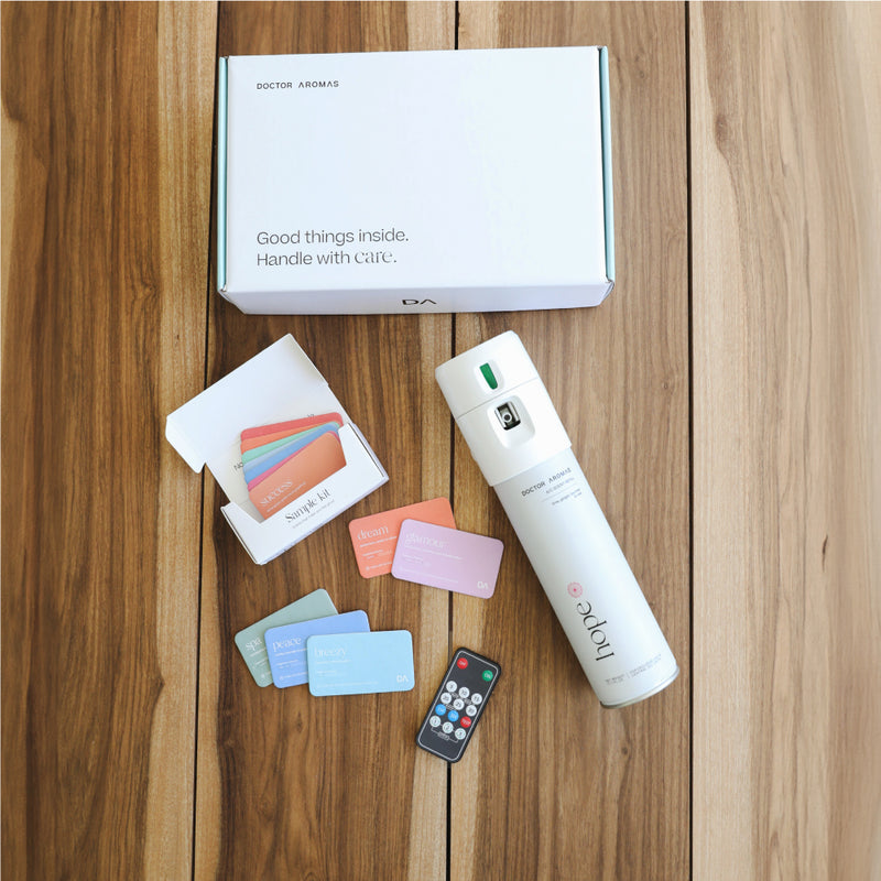 White spray bottle labeled A/C Scenting System with scented cards in pastel colors and a small remote on wooden surface. - A/C Scenting System | Nostalgia - Nostalgia - Doctor Aromas
