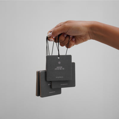 Hand holding three square black pomelo car perfume air fresheners with white text on gray background. - Car Perfume | Pomelo - Pomelo - Doctor Aromas