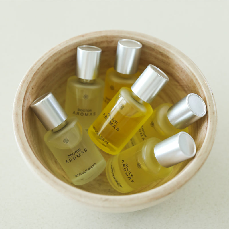 Six small glass bottles with silver caps filled with yellow diffuser oil in a natural wooden bowl. - Diffuser Drops Twin Pack | Holiday - Holiday - Doctor Aromas