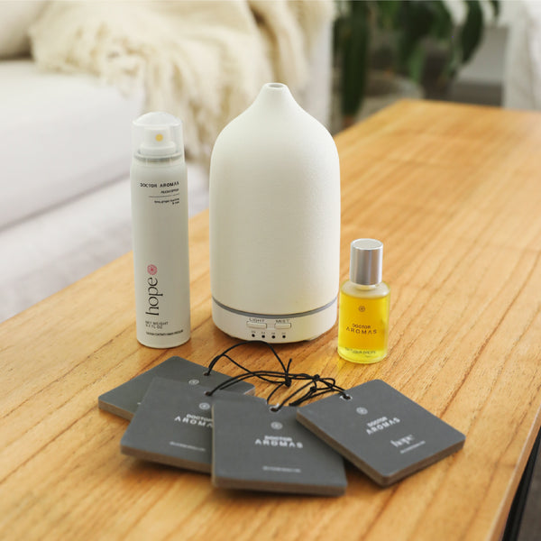 White ceramic essential oil diffuser with a smooth teardrop shape next to a small yellow oil bottle and a tall white spray. - The Gift of HOPE® Deluxe - White - Doctor Aromas