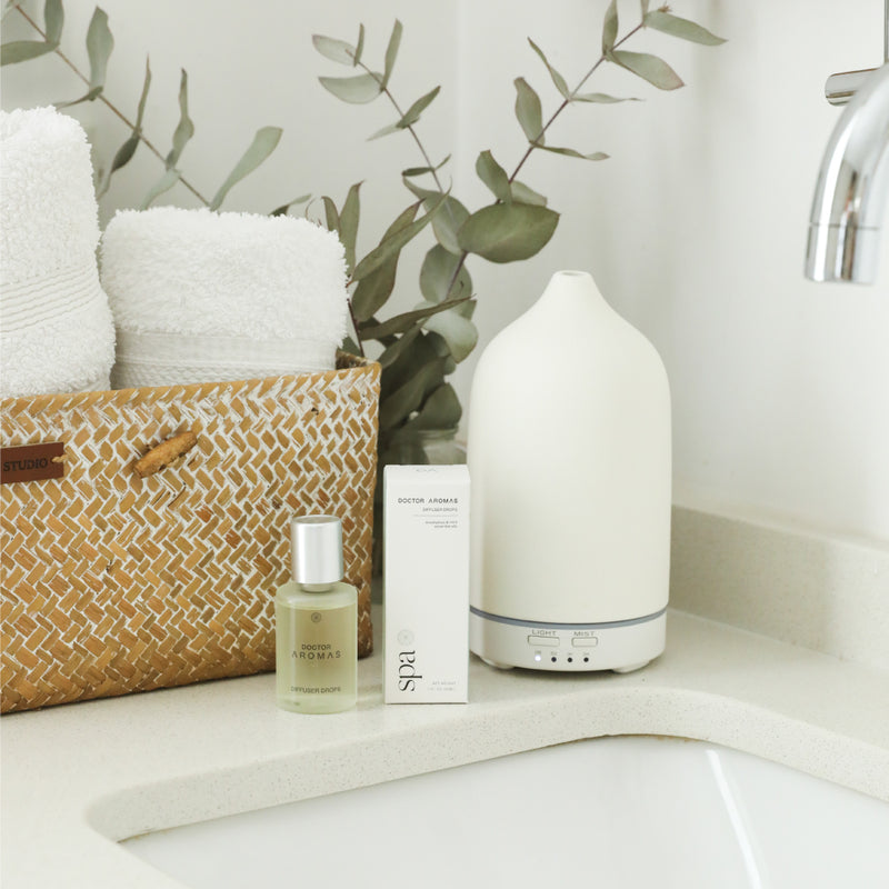 White ceramic aromatherapy stone diffuser with teardrop shape on bathroom counter with eucalyptus and towel basket. - Aromatherapy Stone Diffuser | Holiday - Holiday / White - Doctor Aromas