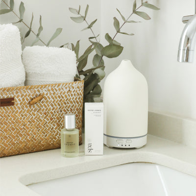 Blush aromatherapy stone diffuser with sleek white base on bathroom counter next to essential oil and woven basket with. - Aromatherapy Stone Diffuser | Blush - Blush / White - Doctor Aromas